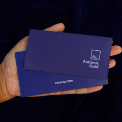 An Automic Gold jewelry polishing cloth laying on top of a blue envelope in a model's hand
