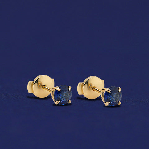 A pair of yellow gold Blue Sapphire Pressure Lock Earrings on a dark blue background