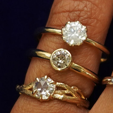 A yellow gold Moissanite Branches Ring, 1/3 Carat Diamond Ring, and a Round Lab Diamond Ring stacked on a model's finger