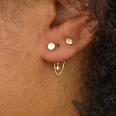 Close up view of a model's ear wearing a yellow gold Diamond Cable Chain Connector across two Circle Studs behind their lobe