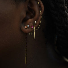 A model's ear wearing a Gemstone Threader, two gemstone studs and a Connector, a Threader, and three Line Earrings