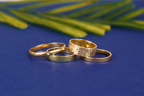 Four Automic Gold wedding bands on a blue background with a large leaf