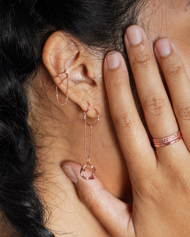 A model wearing various hoops, cuff, rings, and charms all in 14k rose gold