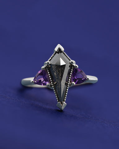 A custom white gold engagement ring with a salt and pepper kite shaped diamond center stone and trillion amethyst side stones