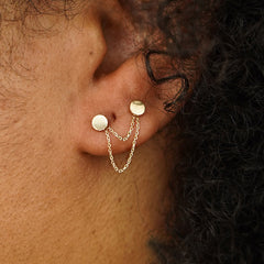 Close up view of a model's ear wearing two Circle Studs with a yellow gold Cable Chain Connector in front of their lobe