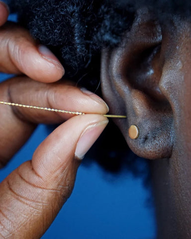 A model inserting a threader into their piercing correctly  by holding the post and keeping the beads straight