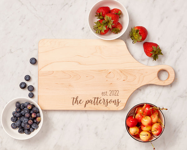 Engraved maple paddle cutting board with berries surrounding it.