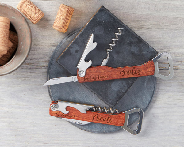 Two engraved wine bottle openers on a slate coaster next to wine corks