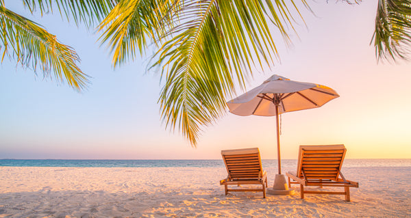 beach sunset with two lounge chairs on the sand under umbrella