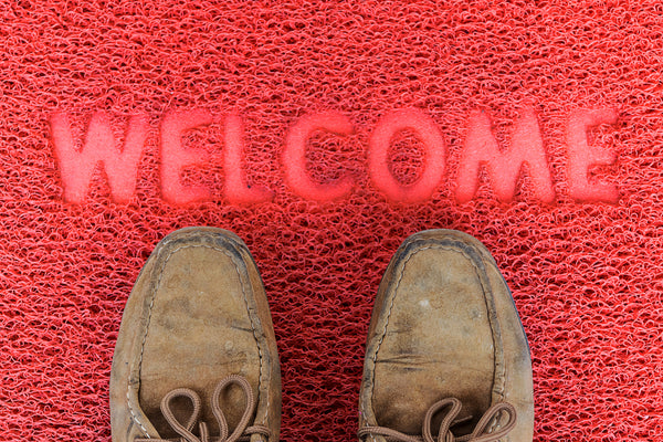 Red welcome mat with brown shoes on it.