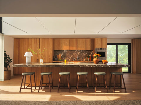 Line up of backless counter stools, walnut base, leather seats on a long stretched out marble countertop kitchen, light walnut walls and cabinets.