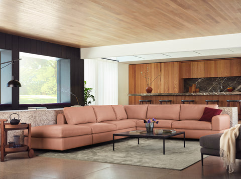 Pink-red sectional with grey rug, black coffee table, red pillow, ruby vase, walnut end table, dark grey chair, and white throw.