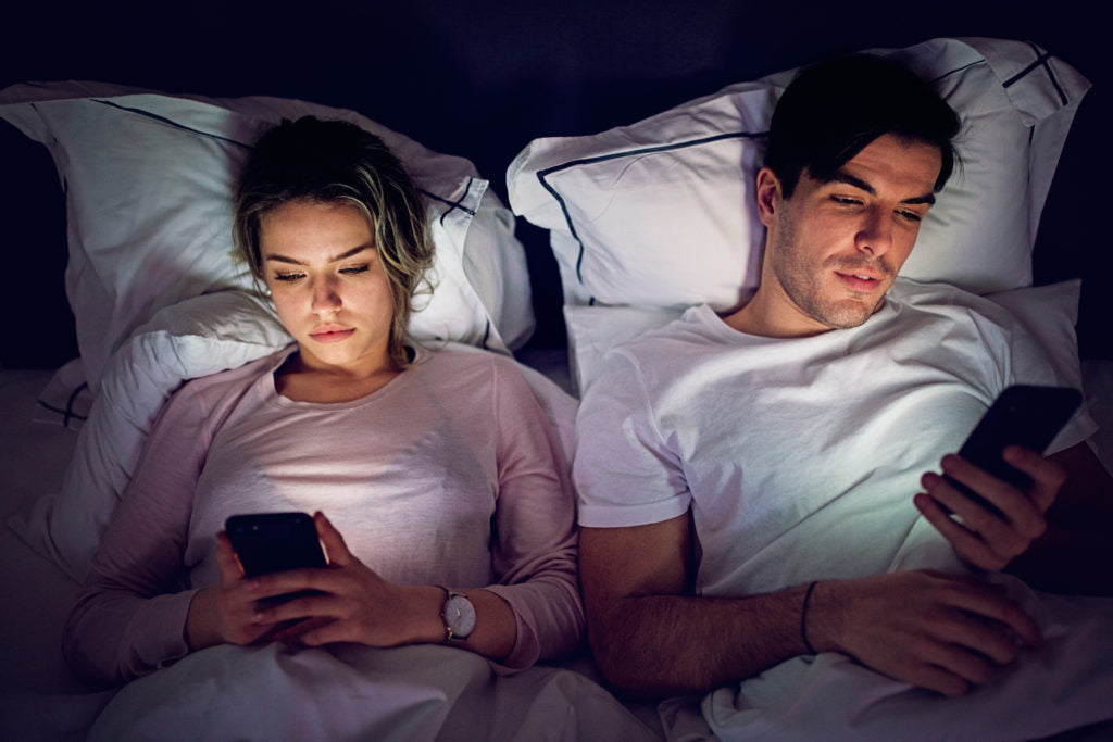 People lying in bed looking at their mobile phones