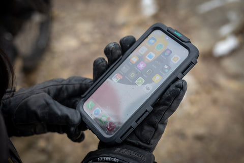 A hand wearing a motorcycle glove holding a phone case, changing the volume of the phone inside.