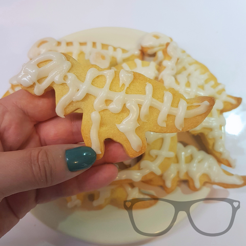 A pale dinosaur shaped cookie being held. the dinosaur is decorated with white piped icing to look like a skeleton