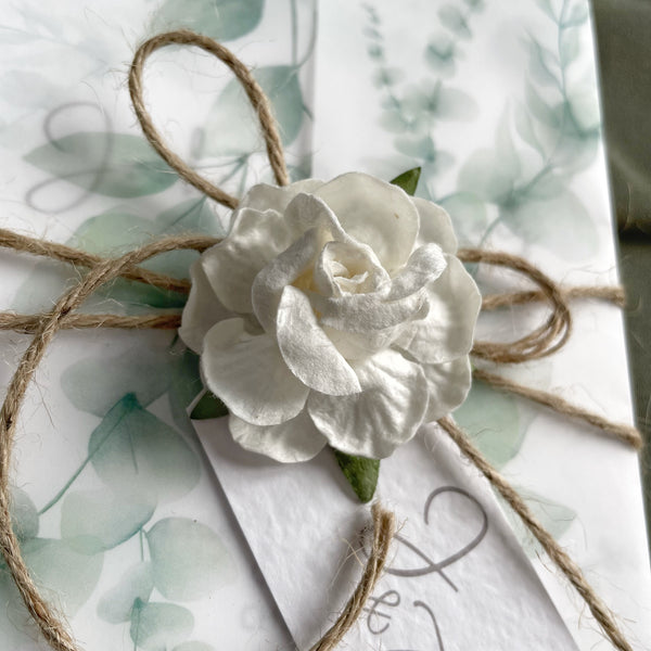 Handmade ivory mulberry paper rose tied with string and used as a belly band on a wedding invitation