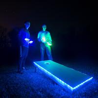 Two people playing cornhole deep into the night using led light up boards. 