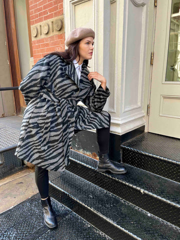 See ROSE Go plus size zebra trench coat on model with one foot one stairs and model leaning on her knee