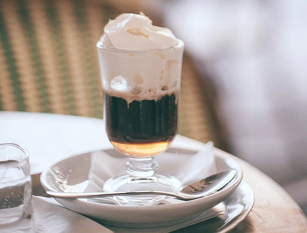 bicchiere con irish coffee con panna con piattino su tavolo