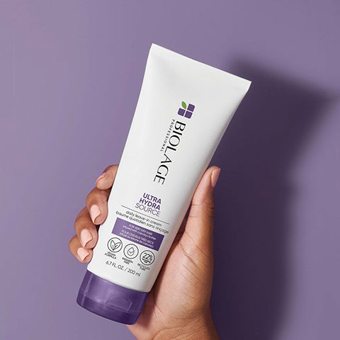 Biolage Ultra Hydra Source Leave In Treatment in hand against purple background