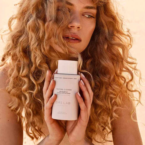 Female with curly hair, holding ORI Lab Restore Cleanse 300ml.