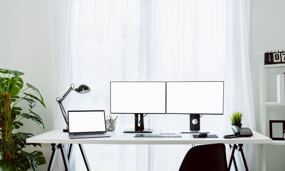 Two computer monitors on a desk, next to a laptop