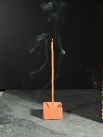 concrete incense burner, incense stick burning with smoke coming from the top, in a dark room with a spotlight on incense