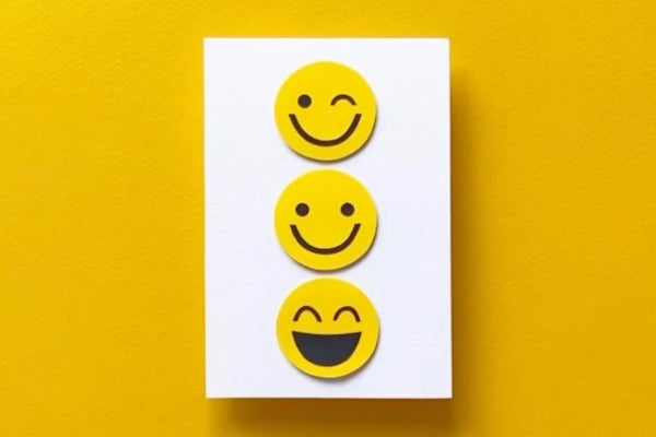 A handmade card with three cutout smiley faces on the front.