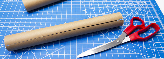 a cardboard tube cut lengthwise next to a pair of scissors on a cutting mat