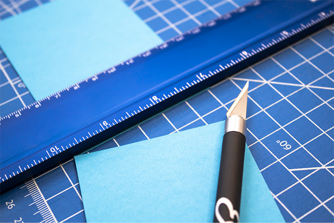 a hobby knife and a ruler on a cutting mat with a piece of construction paper