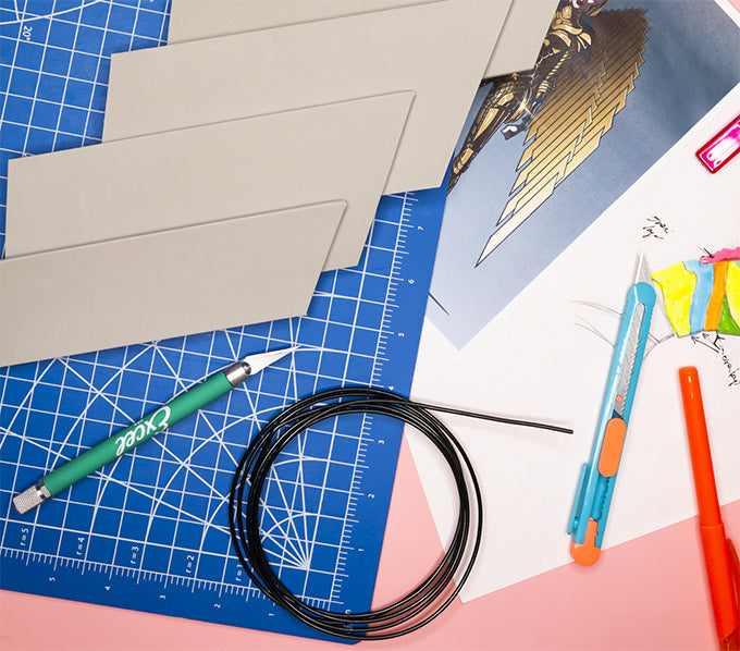 a hobby knife on a cutting mat with pieces of vinyl next to a sketch of a costume