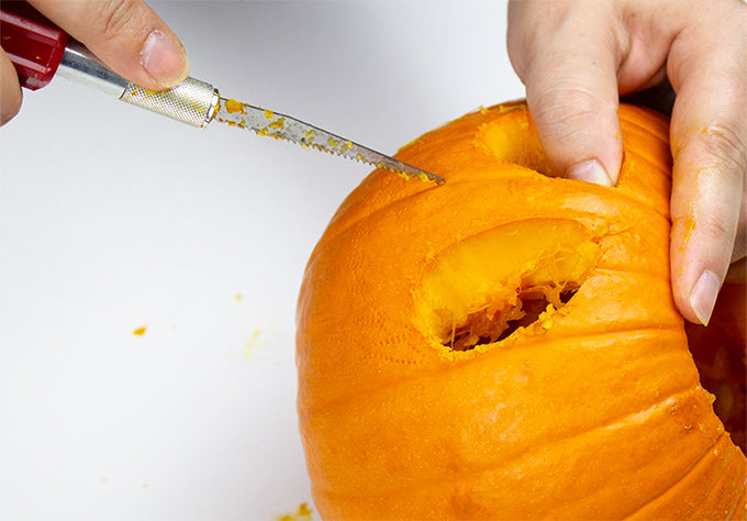 a person carving a pumpkin with a saw blade on a hobby knife