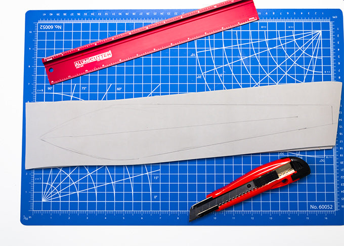 a piece of eva foam with a sword design on it next to a ruler and a snap blade utility knife