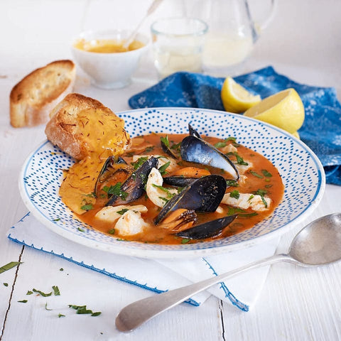 A photo of a bowl of bouillabaisse soup served in a delicate white and blue bowl. 