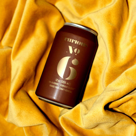 A photo of a brown can of Curious Number 6 laying on yellow velvet.