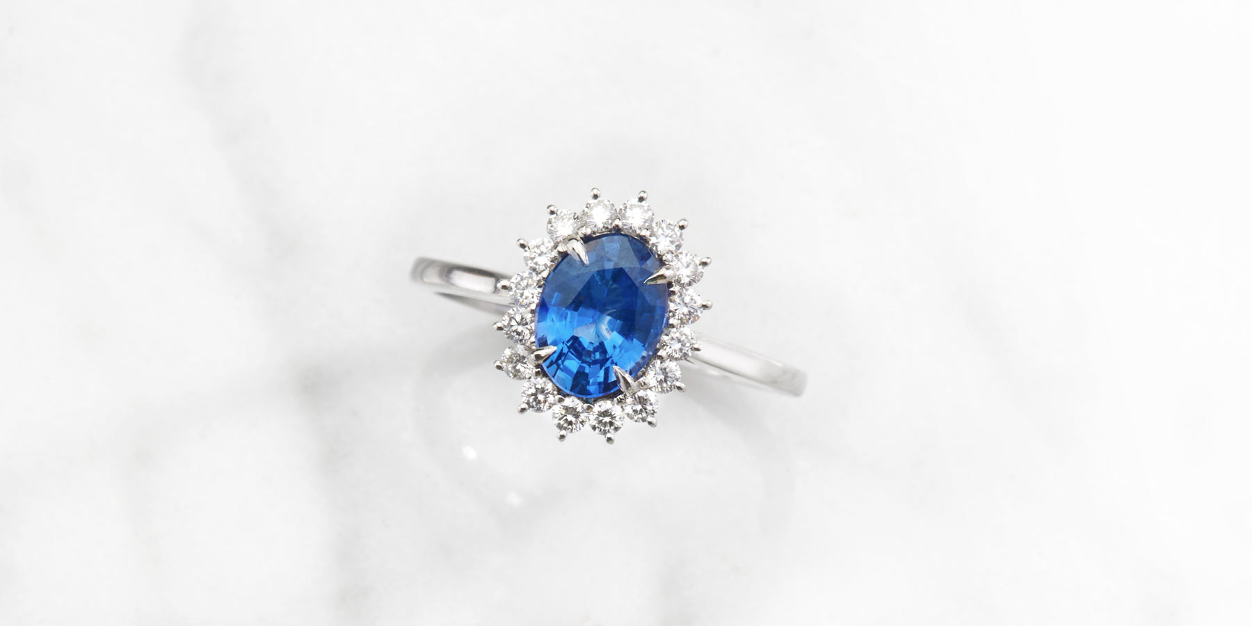  Image nature morte d'une bague étoile taille ovale en saphir bleu vif avec un halo de diamants GH/VS de Fenton | 5 raisons pour lesquelles nous aimons les pierres précieuses plutôt que les diamants avec Fenton