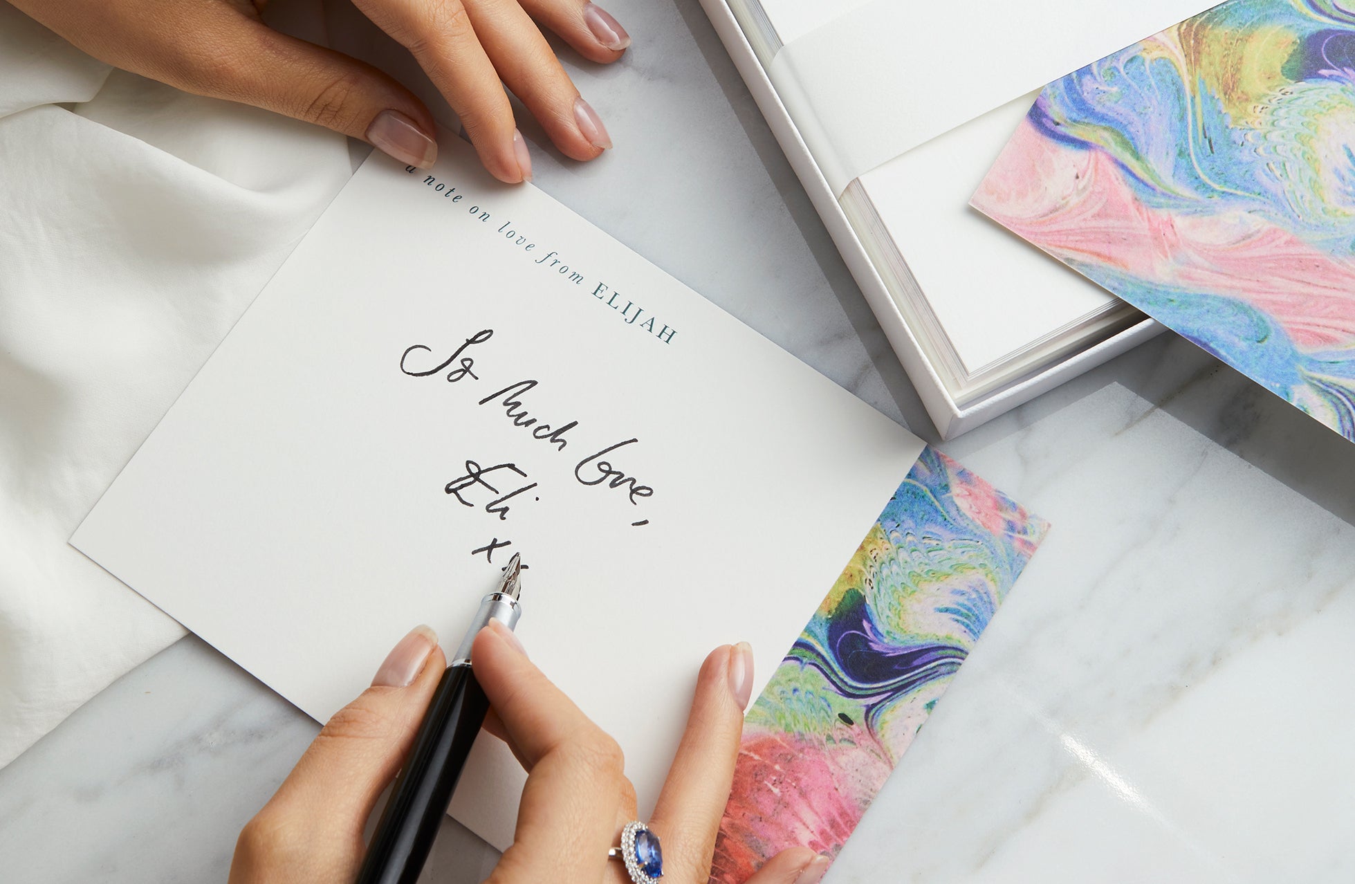 Women wearing a blue sapphire ring and writing a note card on stationary from Fenton x Papier. 
