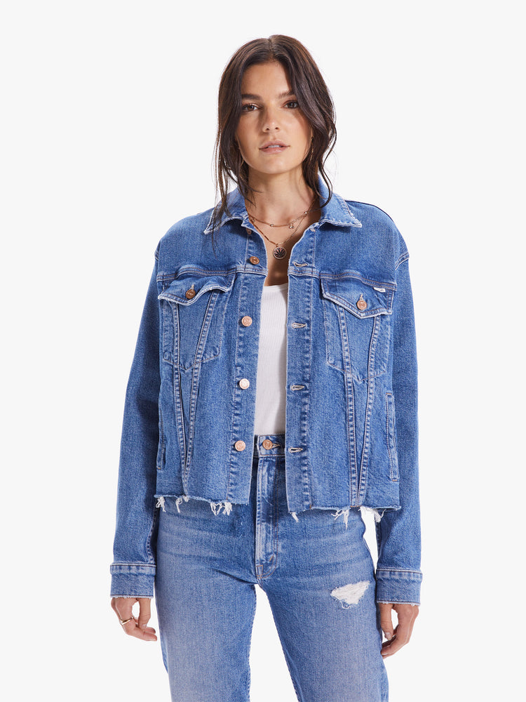 Front view of a woman wearing a medium blue wash denim jacket featuring an oversized fit and a frayed crop hem.