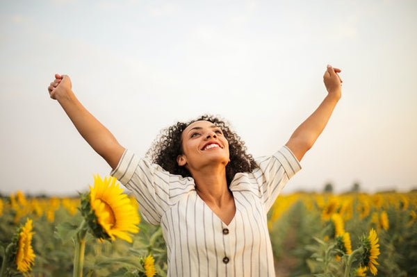woman in sunflower field with hands in air