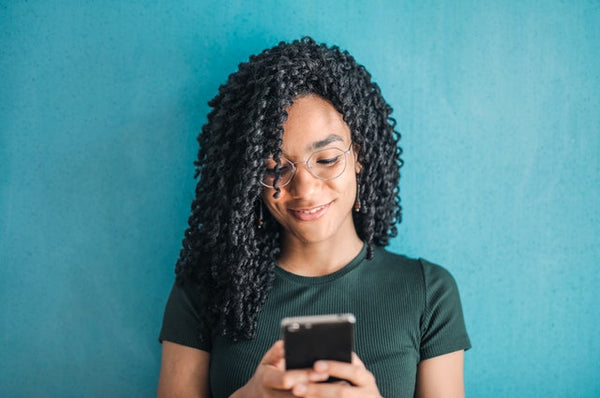 person of color texting in front of blue wall