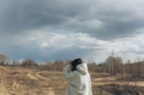 woman looking out into cloudy sky and field 