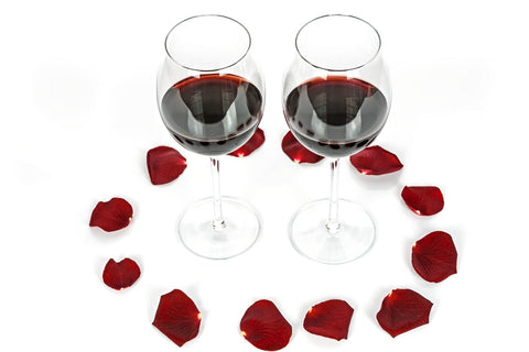Two glasses of wine with rose petals surrounding them