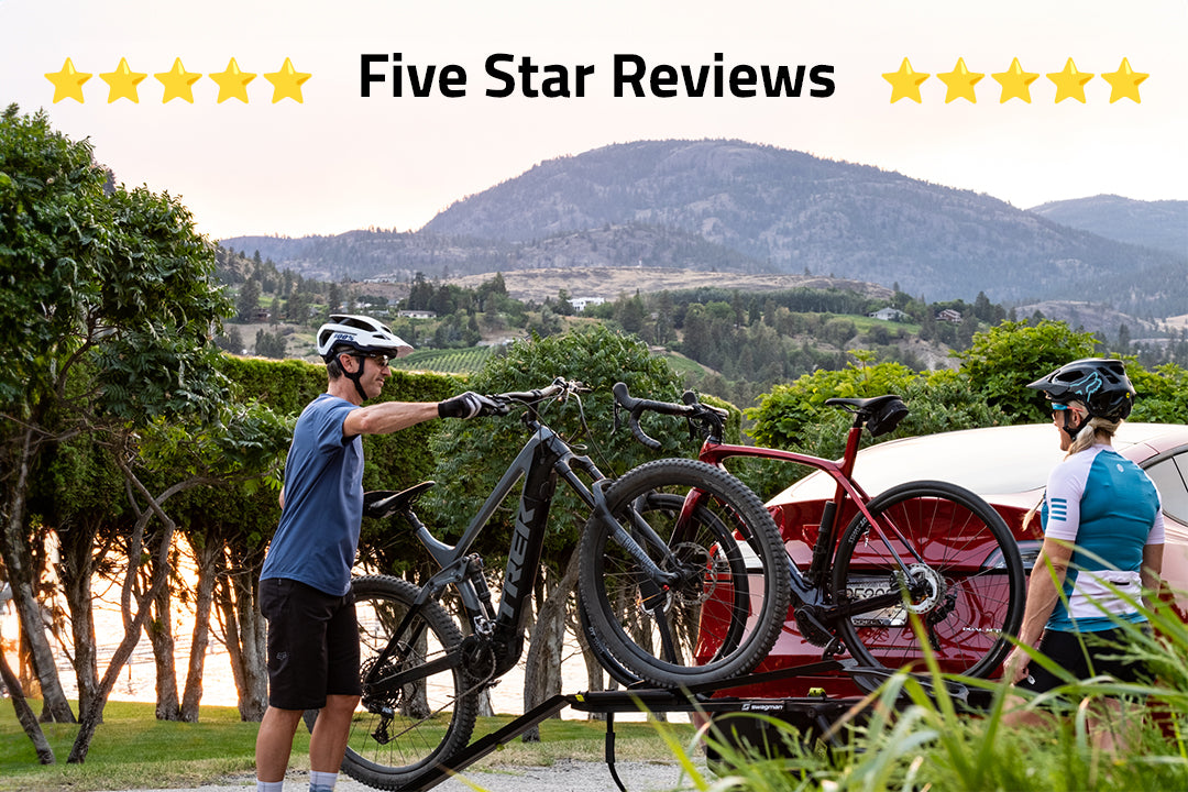 A couple using a ramp and bridge to load an electric mountain bike onto a Swagman Skaha ebike approved hitch rack installed on the back of a Tesla