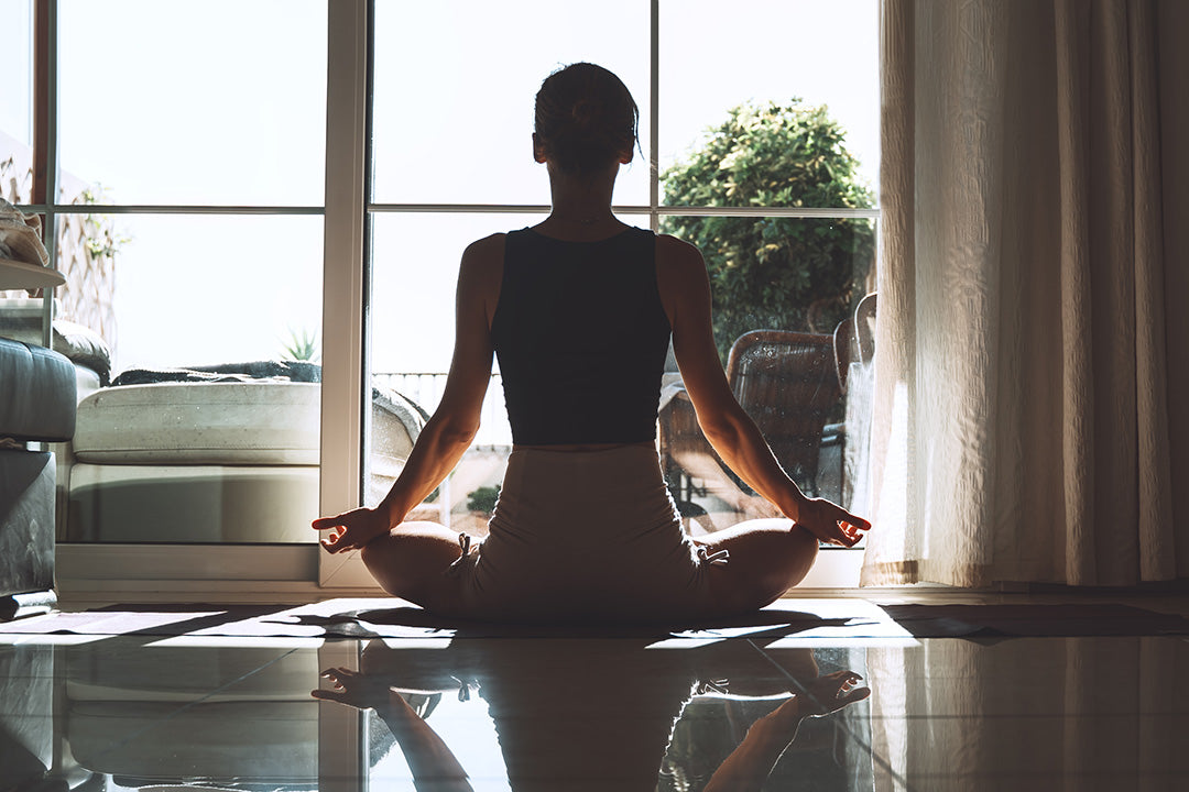 A woman sitting in a yoga pose in front of a sunlit window.