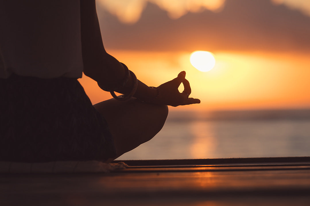 A woman sitting in a cross-legged meditative yoga pose in front of the ocean.