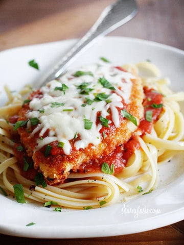 plate of baked chicken parmesan on a bed of pasta noodles