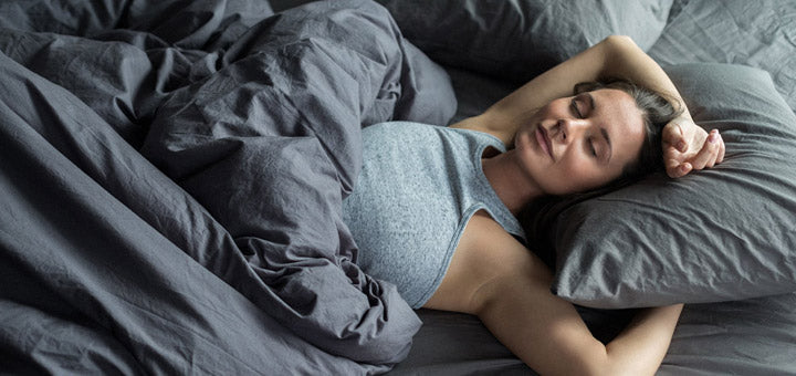 mujer durmiendo en cama con sábanas y almohada plomas