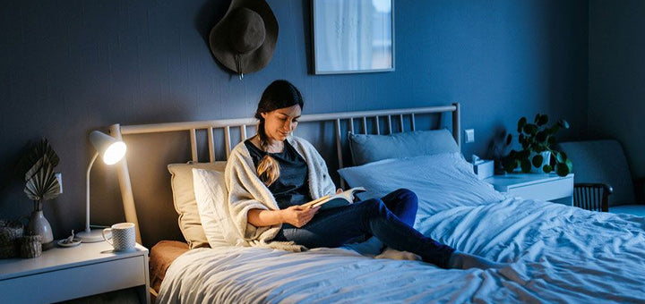 mujer leyendo su libro en su cama con lámpara cuello de cisne
