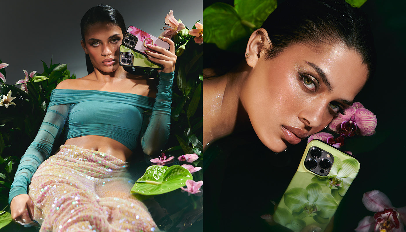 A woman in a teal off-shoulder top and embellished skirt holds smartphones with Secret Garden cases, surrounded by lush greenery and vibrant flowers, showcasing a dramatic makeup look.