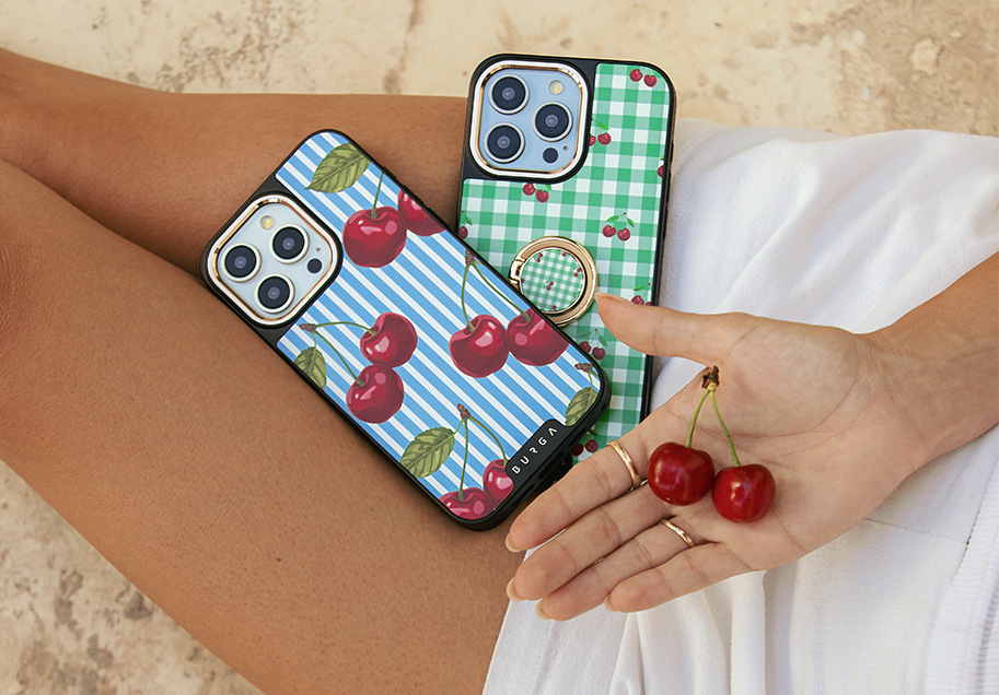 Person holding cherry-patterned smartphone cases and cherries.